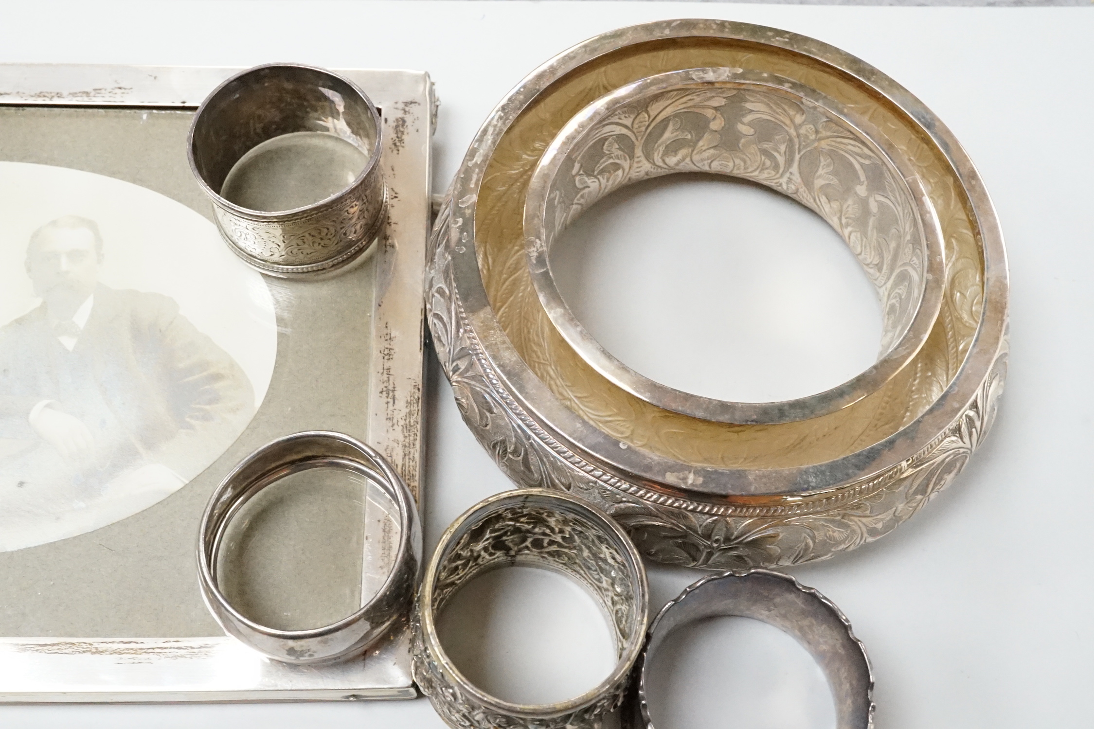 Two George V silver mounted photograph frames including oval, an Indian white metal flower holder and other items including silver napkin rings and a matchbox sleeve.